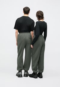 Zöld szabadidőnadrág elasztikus derékpánttal és oldalzsebekkel, fekete felsőkkel párosítva. Lábbeli: masszív fekete tornacipők szürke részletekkel.