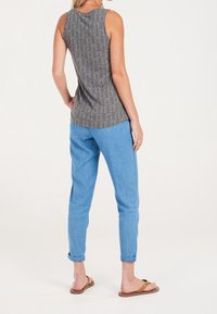 Top de tirantes gris con estampado y dobladillo curvado, combinado con pantalones ajustados azul claro, remangados en los puños, y sandalias planas marrones.