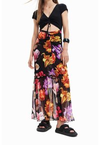 Crop top noir côtelé avec un détail en nœud, associé à une jupe maxi à fleurs superposée dans des couleurs vibrantes. Sandales noires avec des sangles réglables.