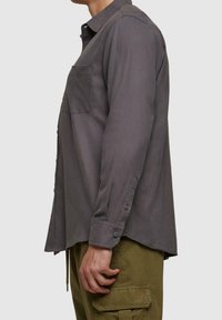 Szara koszula z długim rękawem, kieszenią na piersi, kołnierzykiem zapinanym na guziki oraz mankietami na guziki, w połączeniu z oliwkowozielonymi spodniami typu cargo.