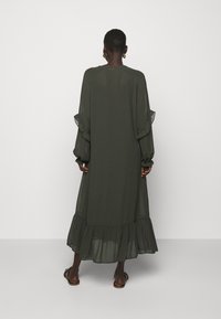 Vestido maxi en verde oscuro, de suave tejido de chiffon, con mangas largas y volantes, y un dobladillo en capas. La espalda descubierta revela una capa transparente.