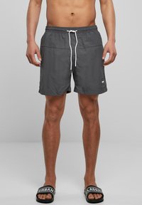 Grå badebukser med snøring i livet, laget av lett materiale. Har sidelommer og en liten merkevarelogo på kanten.