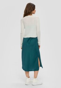 Biały prążkowany top z długim rękawem zestawiony z tealowym satynowym sukienką w kształcie slip z bocznymi rozcięciami oraz białymi, masywnymi sneakersami.