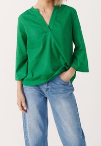 Haut texturé vert avec un col en V, manches trois-quarts et coupe décontractée, associé à un jean droit bleu clair.