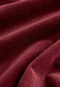 Burgundowa tkanina o gładkiej fakturze, z delikatnymi fałdami i miękkim, pluszowym wyglądem. Brak widocznych wzorów lub elementów metalowych.