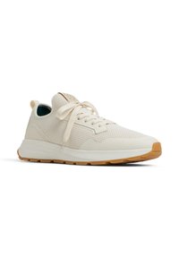 Zapatilla deportiva de un beige claro con un upper de malla texturizada, cordones planos y una suela de goma que presenta un patrón de banda de rodadura marrón. Diseño suave y minimalista.