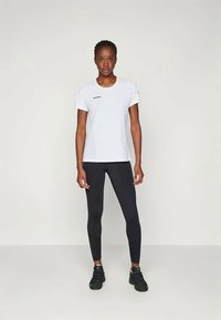 Biesa īsām piedurknēm t-krekls ar mazu logo uz krūtīm, apakšā valkājot melnos legingus un melnas sporta kurpes. Gluda tekstūra, pieguļošs dizains.