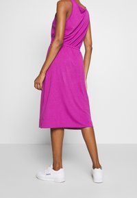 Robe rose sans manches à coupe décontractée, taille cintrée et longueur au genou, associée à des baskets blanches. Texture lisse, design décontracté.