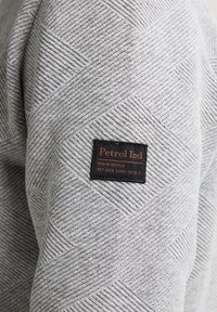 Grijze sweatshirt met textuur, voorzien van een ruitpatroon en een zwart rechthoekig merkembleem met oranje letters op de schouder.