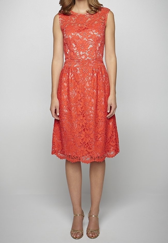 Robe en dentelle corail sans manches longueur genou avec taille ajustée, portée avec des talons ouverts à bride à la cheville dorés sur fond uni.