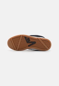 Black sneaker with gum rubber outsole, textured surface, and a patterned grip. Includes black branding detail on the side.