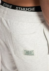 Lichtgrijze sportshorts van een gestructureerde stof, elastische tailleband met zwarte branding, en een zijzak met een labeldetail.