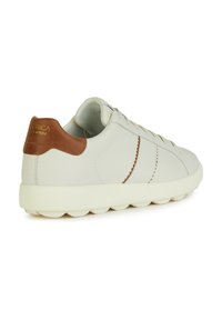 Sneaker bianco in pelle con un accento in pelle marrone sul tallone, cuciture testurizzate e una suola spessa e arrotondata di colore bianco.