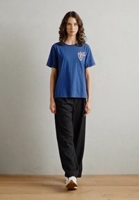 Navy blue cotton t-shirt with short sleeves, featuring a graphic on the left side. Paired with loose black pants and white sneakers.