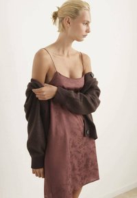 Vestido de satén en mauve con patrón floral, combinado con un cárdigan de punto marrón oscuro, que presenta botones grandes y una tela texturizada.