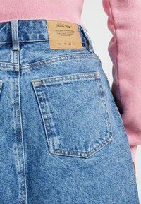 Denimkjol i ljusblått, med hög midja, bakfickor och en brun läderlapp med varumärkesinformation på baksidan.