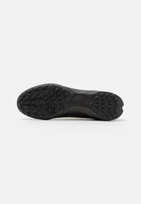 Suela de zapatilla deportiva negra con goma texturizada para tracción, presenta múltiples clavos de agarre y un diseño curvado suave a lo largo de los bordes.