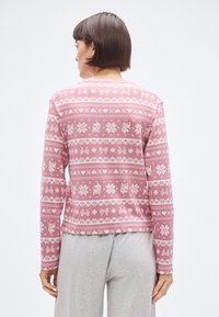 Różowa koszula z długim rękawem, ozdobiona białym wzorem kokardek, płatków śniegu i reniferów. Miękka tkanina, luźny krój i okrągły dekolt.