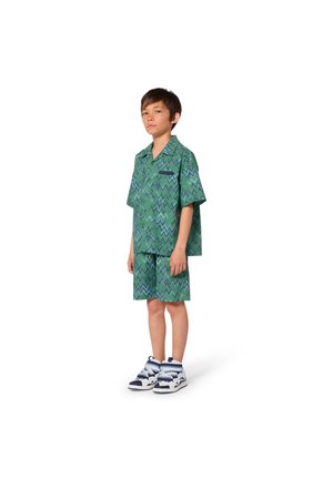 Tenue verte à manches courtes avec motif en zigzag. Chemise carrée et short assorti, associés à des baskets blanches et bleues.