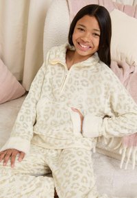 Set de pijamale cu imprimeu leopard dintr-un material moale crem, cu accente aurii. Include un top cu fermoar, guler înalt și manșete pufoase. Design confortabil și cald.