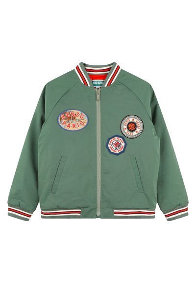 Veste bomber verte avec col et poignets côtelés rayés. Fermeture éclair à l'avant, comportant quatre patchs brodés de différentes couleurs et formes.