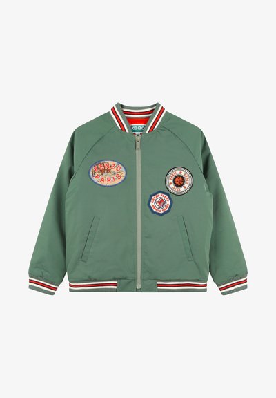 Veste bomber verte avec col et poignets côtelés rayés. Fermeture éclair à l'avant, comportant quatre patchs brodés de différentes couleurs et formes.