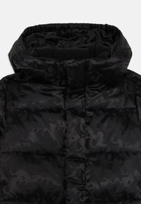 Veste matelassée noire avec un col haut, un motif matelassé et une doublure intérieure douce. Le tissu a un léger éclat et varie en texture.