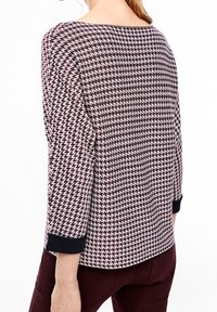 Top en tricot avec un motif pied-de-poule bordeaux et crème, encolure bateau et manches 3/4 avec des poignets noirs. Texture lisse.