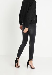 Czarna, prążkowana kurtka bomberka z paskowanym teksturą, w połączeniu z ciemnoszarymi, dopasowanymi dżinsami. Czarne sandały na obcasie z otwartym palcem i detalem w postaci paska wokół kostki.