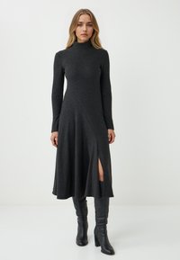 Abito a maglia grigio scuro con maniche lunghe e colletto alto, con orlo asimmetrico e spacco laterale, abbinato a stivali neri con tacco al ginocchio.