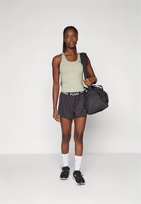 Treeningvarustus, mis sisaldab helerohelisest särk-toppist, mustad lühikesed püksid logoga vöökohal, mustad tossud ja must spordikott.