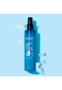 Redken Extreme Anti-Snap-behandling i en blå plastsprayflaska, med ett svart munstycke, omgiven av bubblor på en ljusblå bakgrund.