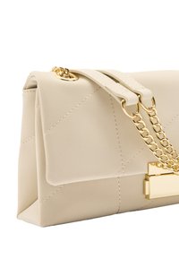 Beżowa torebka skórzana z pikowaniem, z złotym łańcuszkiem oraz prostokątnym złotym zapięciem, widok pod kątem na białym tle.