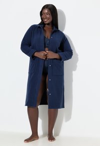 Tmavě modrý fleecový župan s kapucí, zapínáním na knoflíky, dvěma bočními kapsami a zipovým detailem vpředu. Měkká textura, celoplošný design.