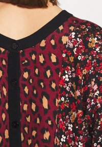 Cardigan lavorato a maglia con bottoni neri, caratterizzato da una stampa leopardata bordeaux e beige su un lato e da un motivo floreale scuro sull'altro.
