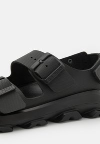 Mustad mustad kaks reguleeritavat rihma, valmistatud tekstuuritud materjalist. Omab paksu tallaga, millel on silmapaistvad mustrid ja reljeefne brändingu logo.