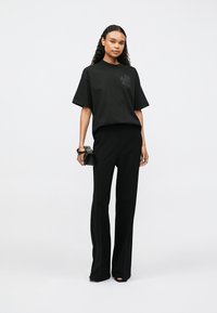 Černé oversized tričko s jemným grafikou, spojené s vysokým pasem černých kalhot, vytvářející elegantní monochromatický outfit.