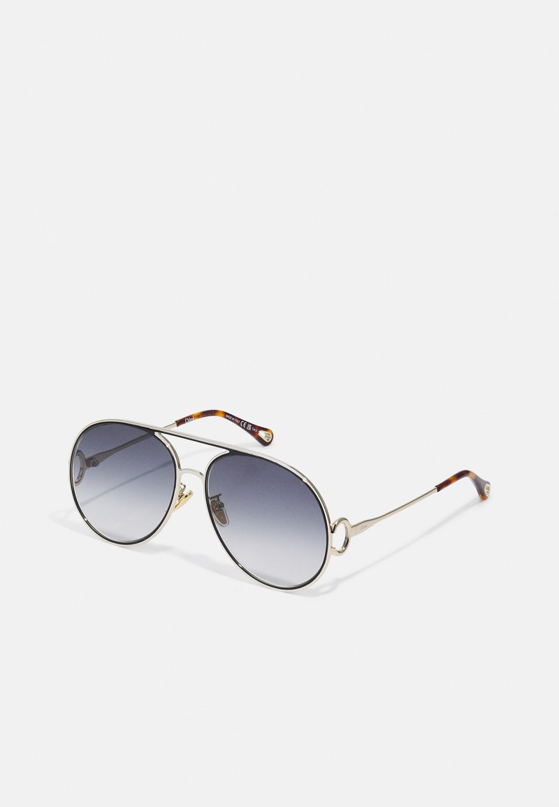Óculos de sol ovais com uma armação de metal dourado, lentes cinza degradê e pontas com padrão tartaruga nas hastes. Almofadas de nariz ajustáveis.