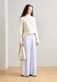 Pull en col roulé beige côtes, pantalon taille haute à large jambe en bleu clair avec un motif floral, et un petit sac à main crème.