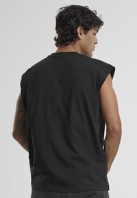 T-shirt sans manches noir au fit décontracté, avec un col rond et une texture lisse, présenté de dos.