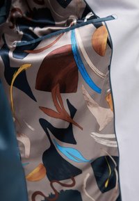 Multicolored satin fabric features abstract shapes in browns, blues, and golds, with a smooth texture and a contrasting blue edge.