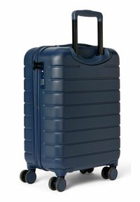 Valise bleu marine à surface texturée, rainures horizontales, poignée rétractable et quatre roues rondes pour la mobilité. Fermeture éclair sécurisée avec serrure.