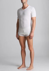 T-shirt bianco attillato a maniche corte, in tessuto morbido, design collo rotondo, texture liscia, abbinato a slip bianchi coordinati, modello in piedi a piedi nudi.