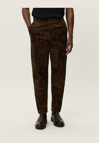 Pantaloni din corduroy maro cu o textură subtilă, design cu picior drept și închidere cu buton frontal. Asortați cu ghete negre până la gleznă.