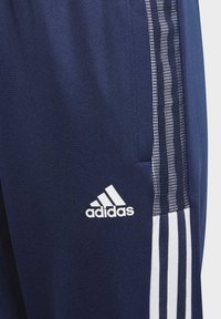 Pantalones deportivos de color azul marino con tejido texturizado, que presentan el logo blanco de Adidas y tres franjas verticales blancas a lo largo de un lado.