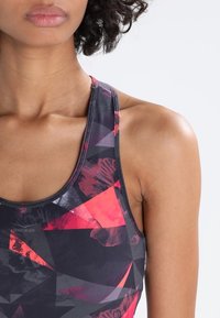 Wielokolorowy sportowy tank top z geometrycznym wzorem w odcieniach czerni, czerwieni i fioletu, z wysokim dekoltem i tyłem typu racerback.