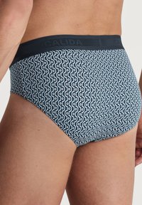 Calida herenonderbroek in donkerblauw met een golvend patroon in lichtblauw. Kenmerkt zich door een donkere tailleband met ingedrukte branding. Gemaakt van katoen.
