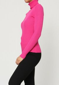 Pull col roulé ajusté en tissu côtelé rose vif, manches longues et silhouette près du corps, associé à un legging noir.