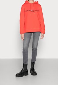 Rode hoodie met Tommy Hilfiger-logo, gecombineerd met grijze skinny jeans en zwarte enkellaarsjes met dikke zolen. Eenvoudig ontwerp.