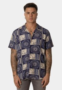 Camisa de manga corta en azul marino con patrones crema. Presenta diseños circulares y formas geométricas; tela ligera con un corte holgado.